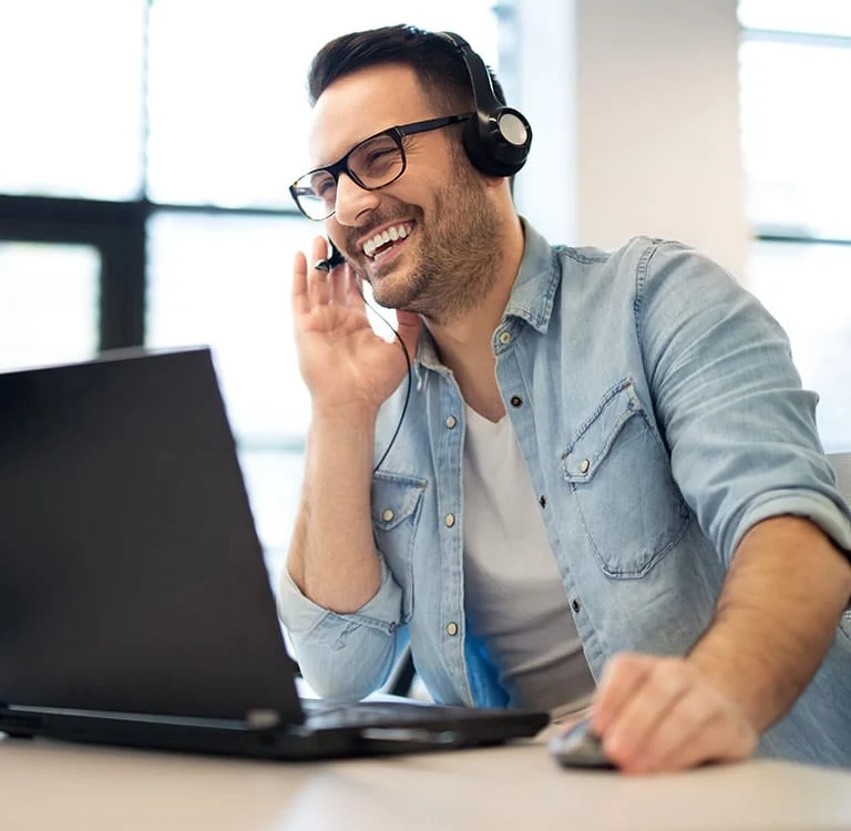 man with headset smiling and looking at computer