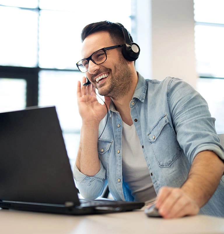 man with headset smiling and looking at computer